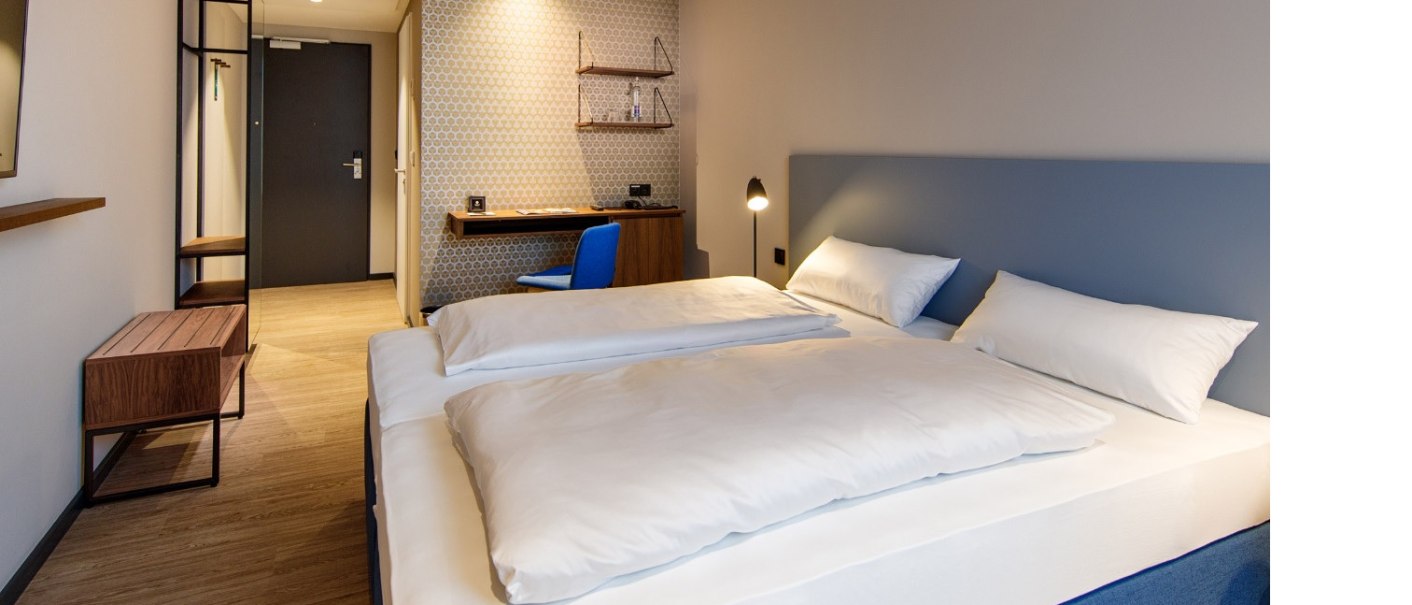 Modern hotel room with double bed, desk, blue chair and stylish lighting. Subtle wallpaper and wooden furniture complete the design., © Arthotel ANA Momentum Modern hotel room with double bed, desk, blue chair and stylish lighting. Subtle wallpaper and wooden furniture complete the design., © Arthotel ANA Momentum