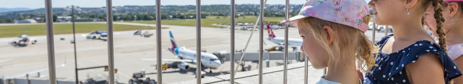 Kinder stehen auf der Besucherterrasse des Stuttgarter Flughafens und schauen durch ein Gitter auf das Rollfeld mit Flugzeugen., &copy; Flughafen Stuttgart