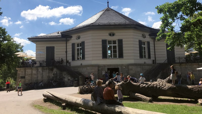 The Bärenschlössle in Stuttgart, surrounded by trees, with people relaxing and playing outside in the sunny weather., © SMG