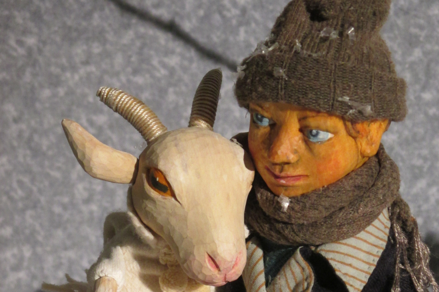 Eine Holzfigur eines Jungen hält eine Ziege im Arm. Beide tragen winterliche Kleidung, der Junge hat einen Schal und eine Mütze an., © Figurentheater Weidringer Eine Holzfigur eines Jungen hält eine Ziege im Arm. Beide tragen winterliche Kleidung, der Junge hat einen Schal und eine Mütze an., © Figurentheater Weidringer
