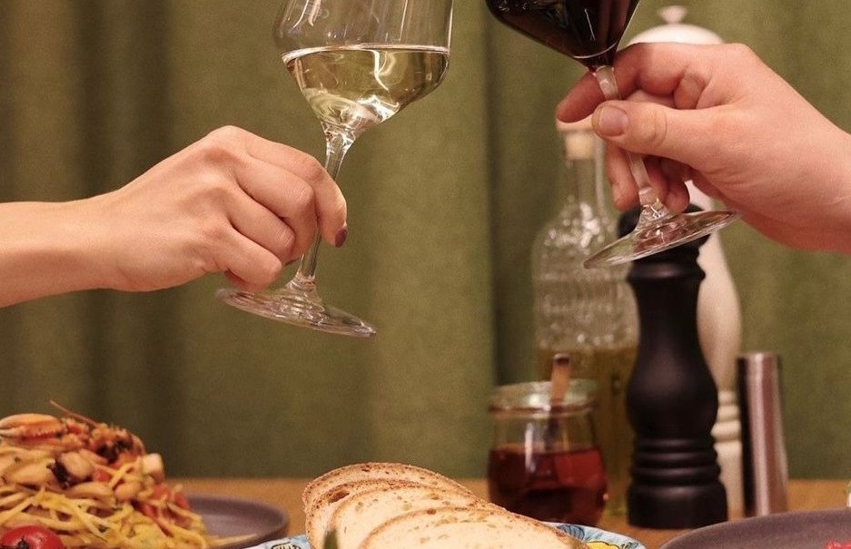 Two people toast with glasses of white and red wine, surrounded by pasta, bread and vegetable dishes on a table., &copy; Roberts