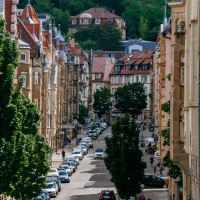 Eine belebte Stadtstraße mit geparkten Autos, alten Gebäuden und Bäumen. Im Hintergrund sind Hügel und weitere Häuser zu sehen., © Thomas Niedermüller Eine belebte Stadtstraße mit geparkten Autos, alten Gebäuden und Bäumen. Im Hintergrund sind Hügel und weitere Häuser zu sehen., © Thomas Niedermüller