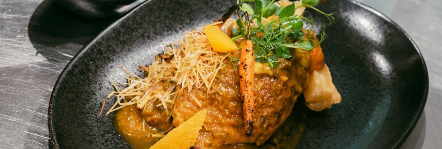 An artfully arranged dish on a black plate, garnished with vegetables, herbs and a sauce. A bowl of salad in the background., &copy; � 2024 Ohh halla, all rights reserved.