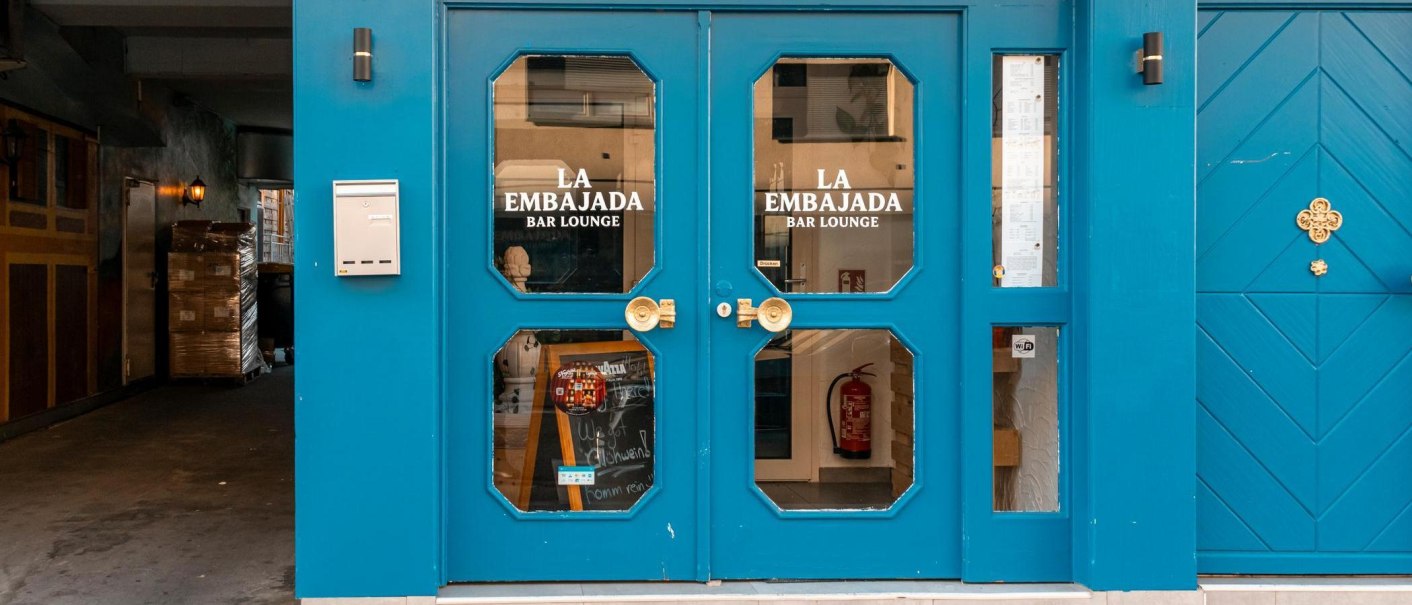 Gro&szlig;e Doppelt&uuml;r in leuchtendem Blau mit Glaseins&auml;tzen, auf denen "La Embajada Bar Lounge" in wei&szlig;en Lettern geschrieben steht., &copy; SMG Stuttgart Marketing GmbH - Sarah Schmid