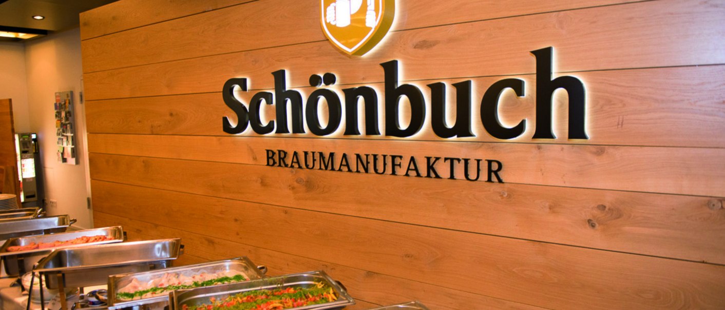 Interior view of a brewery with buffet. "Schönbuch Braumanufaktur" is written on the wooden wall. In the foreground are dishes in warming containers., © © Schönbuchbrauerei, Sebastian Berger Interior view of a brewery with buffet. "Schönbuch Braumanufaktur" is written on the wooden wall. In the foreground are dishes in warming containers., © © Schönbuchbrauerei, Sebastian Berger