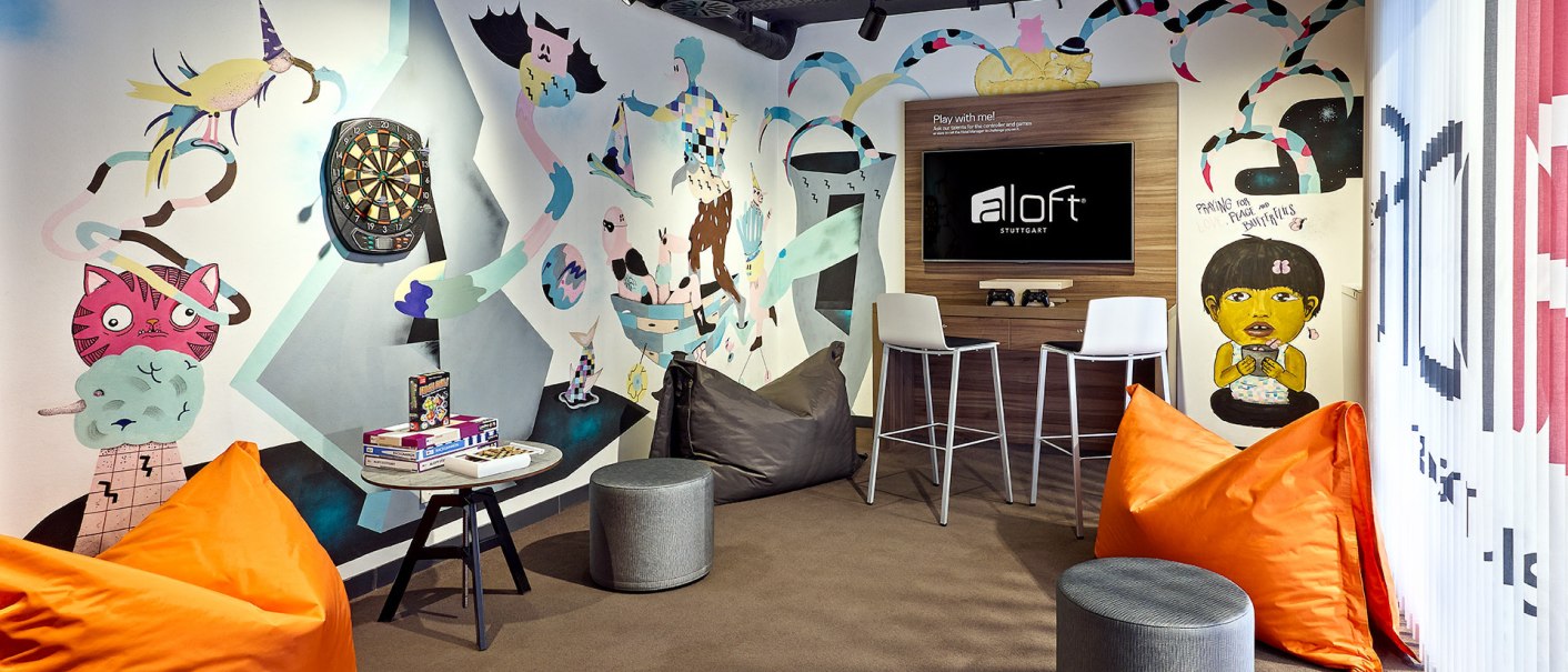 Ein bunter Gaming-Raum mit Wandmalereien, Sitzsäcken, einem Fernseher und einem Dartboard. Perfekt zum Entspannen und Spielen., © aloft Stuttgart Ein bunter Gaming-Raum mit Wandmalereien, Sitzsäcken, einem Fernseher und einem Dartboard. Perfekt zum Entspannen und Spielen., © aloft Stuttgart