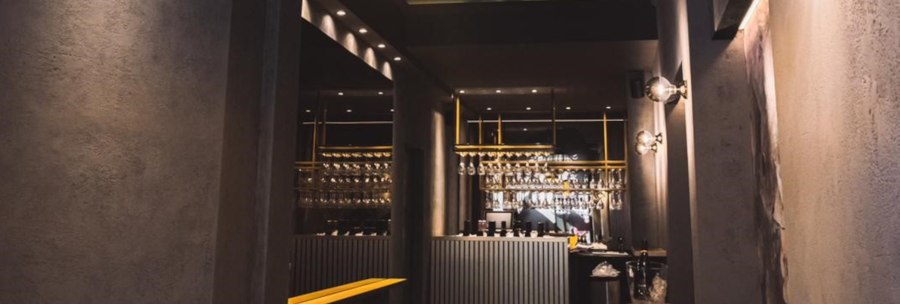 Stylish bar with a modern design, hanging glasses and elegant lighting. The counter is positioned in the center, surrounded by dark walls., &copy; KESSLER Sekt GmbH & Co. KG