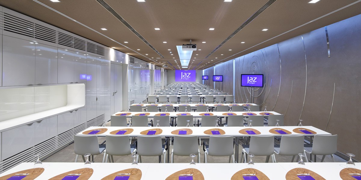 Modern conference room with white tables and chairs, screens on the walls and a projector on the ceiling., © Jaz Hotel Stuttgart Modern conference room with white tables and chairs, screens on the walls and a projector on the ceiling., © Jaz Hotel Stuttgart