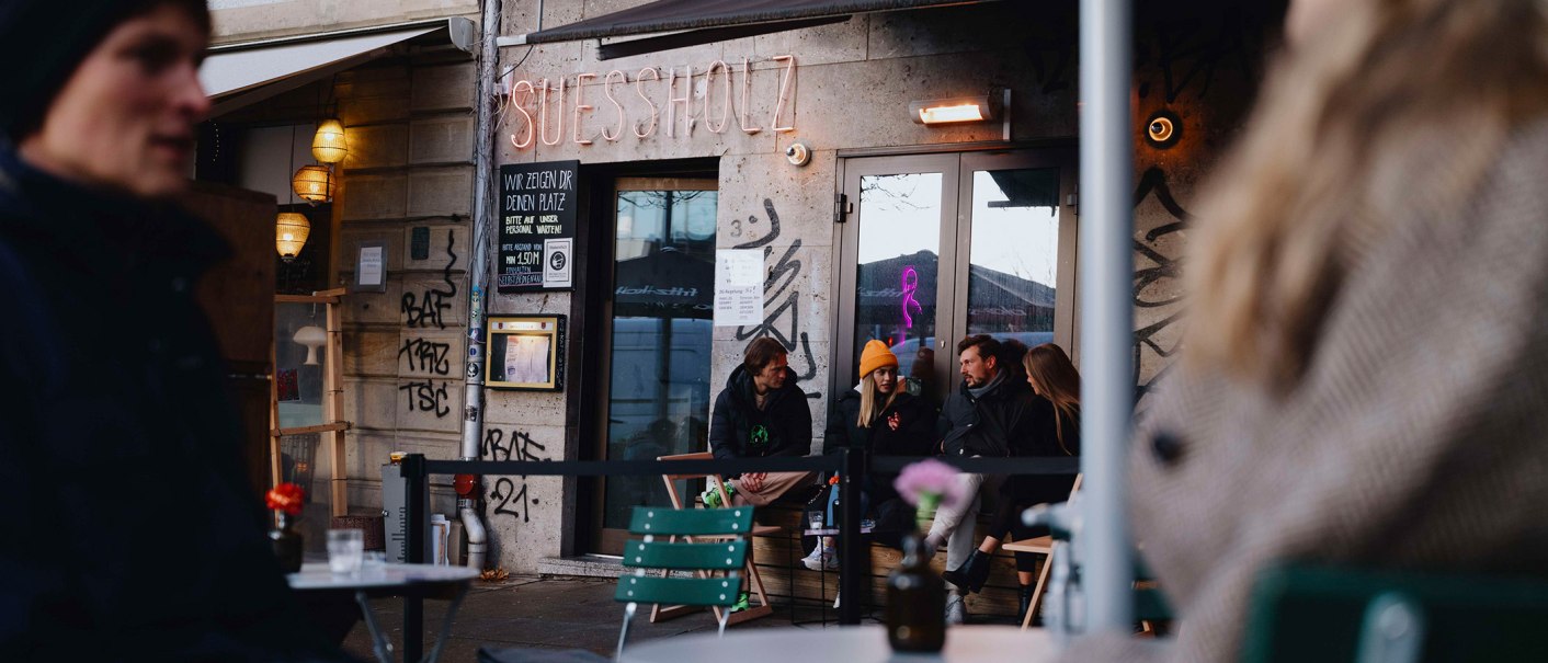Au&szlig;enansicht des Caf&eacute;s 'Suessholz' im Leonhardsviertel. Menschen sitzen drau&szlig;en, unterhalten sich. Graffiti an den W&auml;nden, Neonlicht im Fenster., &copy; Stuttgart-Marketing GmbH, Alwin Maigler