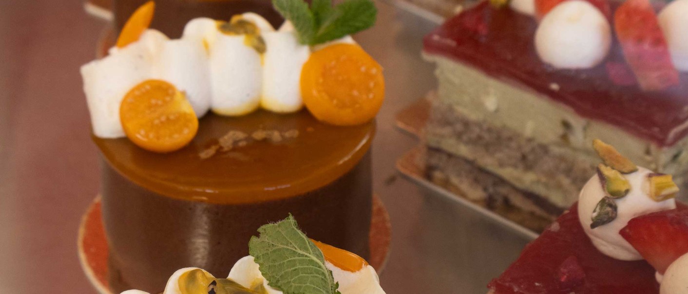 Close-up of artfully decorated cakes in a display case. Various toppings such as fruit and cream can be seen., © SMG