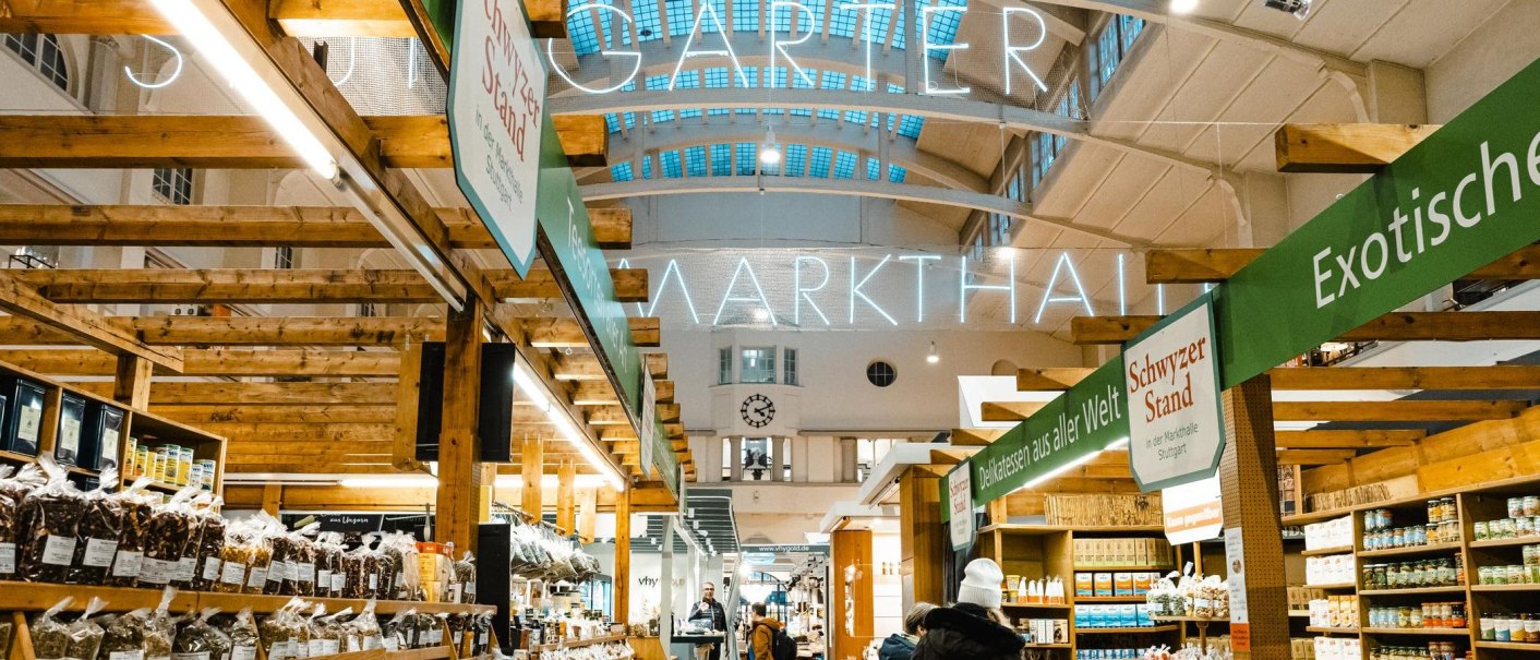 Interior view of the Stuttgart market hall with wooden stalls, illuminated signage and various delicatessen stalls., © by Canto