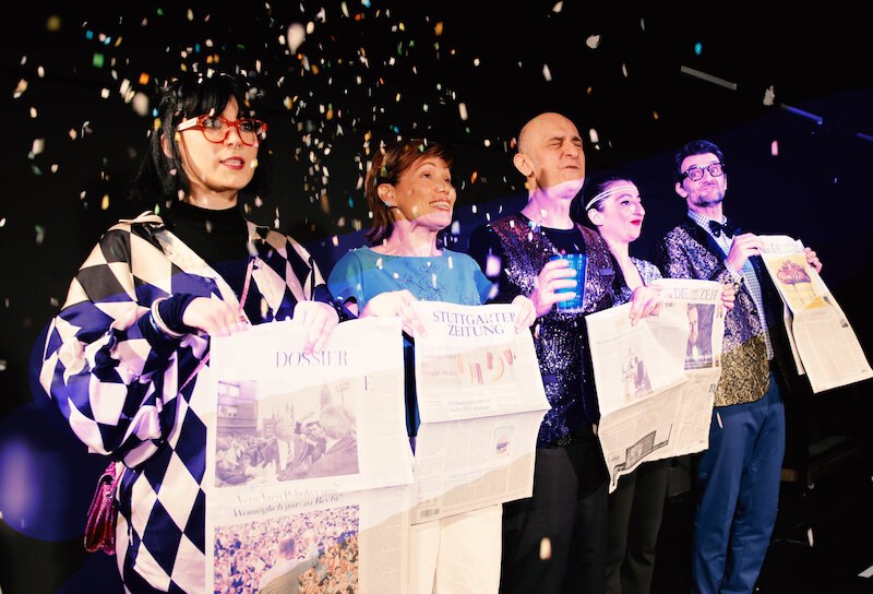 F&uuml;nf Personen auf einer B&uuml;hne halten Zeitungen und sind von Konfetti umgeben. Sie wirken fr&ouml;hlich und festlich gekleidet., &copy; tri-b&uuml;hne e.V.