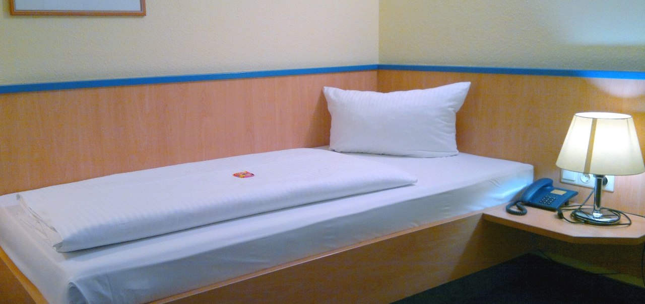 Ein schlichtes Einzelzimmer mit Bett, Nachttisch, Lampe und Telefon. An der Wand h&auml;ngt ein Bild., &copy; Central Hotel