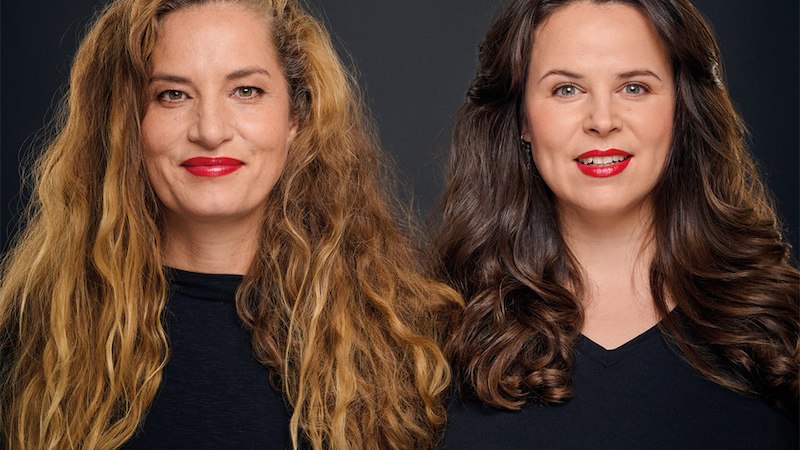 Zwei Frauen mit langen Haaren und roten Lippen posieren vor einem dunklen Hintergrund. Beide tragen schwarze Oberteile., © Rosenau Kultur e.V. Zwei Frauen mit langen Haaren und roten Lippen posieren vor einem dunklen Hintergrund. Beide tragen schwarze Oberteile., © Rosenau Kultur e.V.