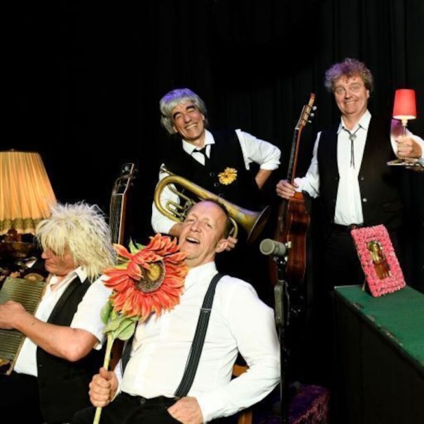 Vier Männer in schwarzer Kleidung posieren mit Musikinstrumenten und Requisiten auf einer Bühne. Einer hält eine große Blume., © Theaterhaus Stuttgart e.V. Vier Männer in schwarzer Kleidung posieren mit Musikinstrumenten und Requisiten auf einer Bühne. Einer hält eine große Blume., © Theaterhaus Stuttgart e.V.