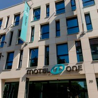 Modern façade of a building with Motel One logo and blue flag waving in the wind. Clear lines and large windows characterize the design., © Motel One Stuttgart-Bad Cannstatt