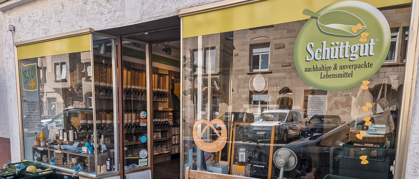 Außenansicht eines Unverpackt-Ladens mit Schüttgut-Logo. Im Schaufenster sind Behälter mit Lebensmitteln und ein Schild mit "BIO" zu sehen., © Schüttgut, Stuttgart