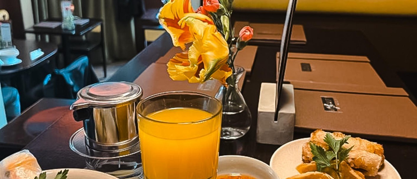 Asian dishes on a table: spring rolls, dumplings, rice, vegetables and a glass of orange juice. A cozy restaurant ambience in the background., © by Canto