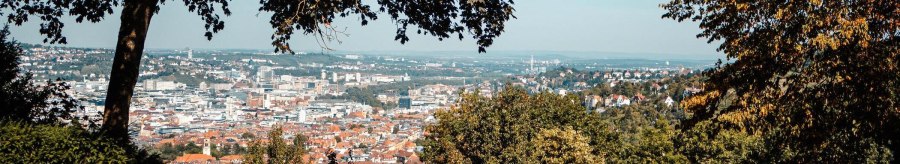 Panoramablick auf eine Stadt mit B&auml;umen im Vordergrund, die den Blick einrahmen. Eine Person sitzt auf einer Bank und genie&szlig;t die Aussicht., &copy; Stuttgart-Marketing GmbH, Sarah Schmid