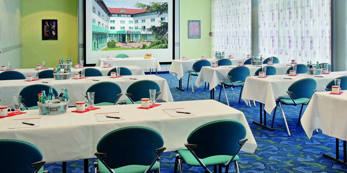 A conference room with set tables, chairs and a large screen. Bottles of water and glasses are provided., © © H-Hotels.com A conference room with set tables, chairs and a large screen. Bottles of water and glasses are provided., © © H-Hotels.com