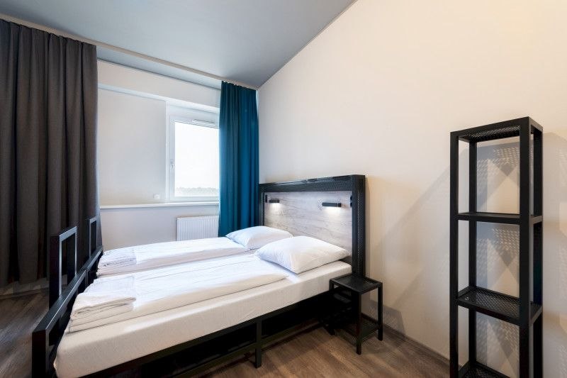 Modern double room with two single beds, a small bedside table and a shelf. Light walls and curtains in blue and gray., © A&O Hostels Marketing GmbH Modern double room with two single beds, a small bedside table and a shelf. Light walls and curtains in blue and gray., © A&O Hostels Marketing GmbH