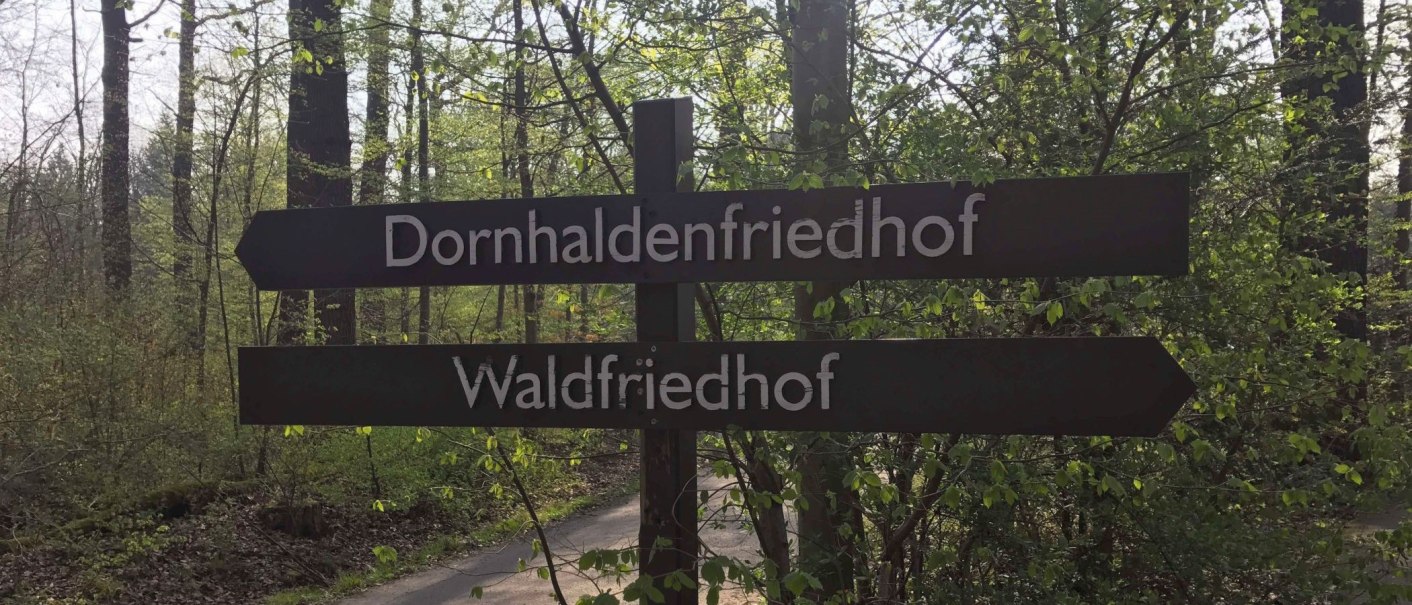Wegweiser im Wald zeigt zu Dornhaldenfriedhof und Waldfriedhof. Umgeben von Bäumen und grünem Laub., © Stuttgart-Marketing GmbH