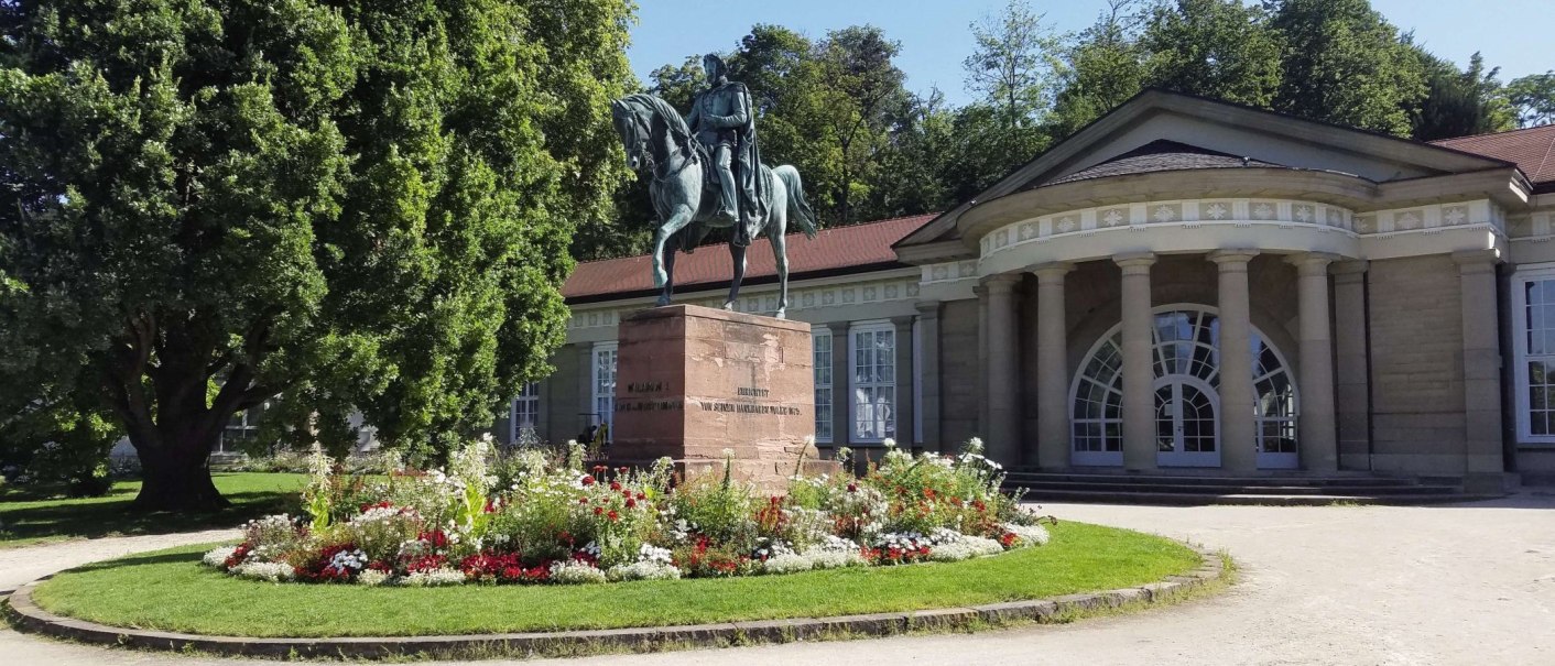 Reiterstatue vor dem Kursaal Bad Cannstatt, umgeben von einem Blumenbeet und großen Bäumen. Das Gebäude hat eine runde Fassade mit Säulen., © Stuttgart-Marketing GmbH Reiterstatue vor dem Kursaal Bad Cannstatt, umgeben von einem Blumenbeet und großen Bäumen. Das Gebäude hat eine runde Fassade mit Säulen., © Stuttgart-Marketing GmbH