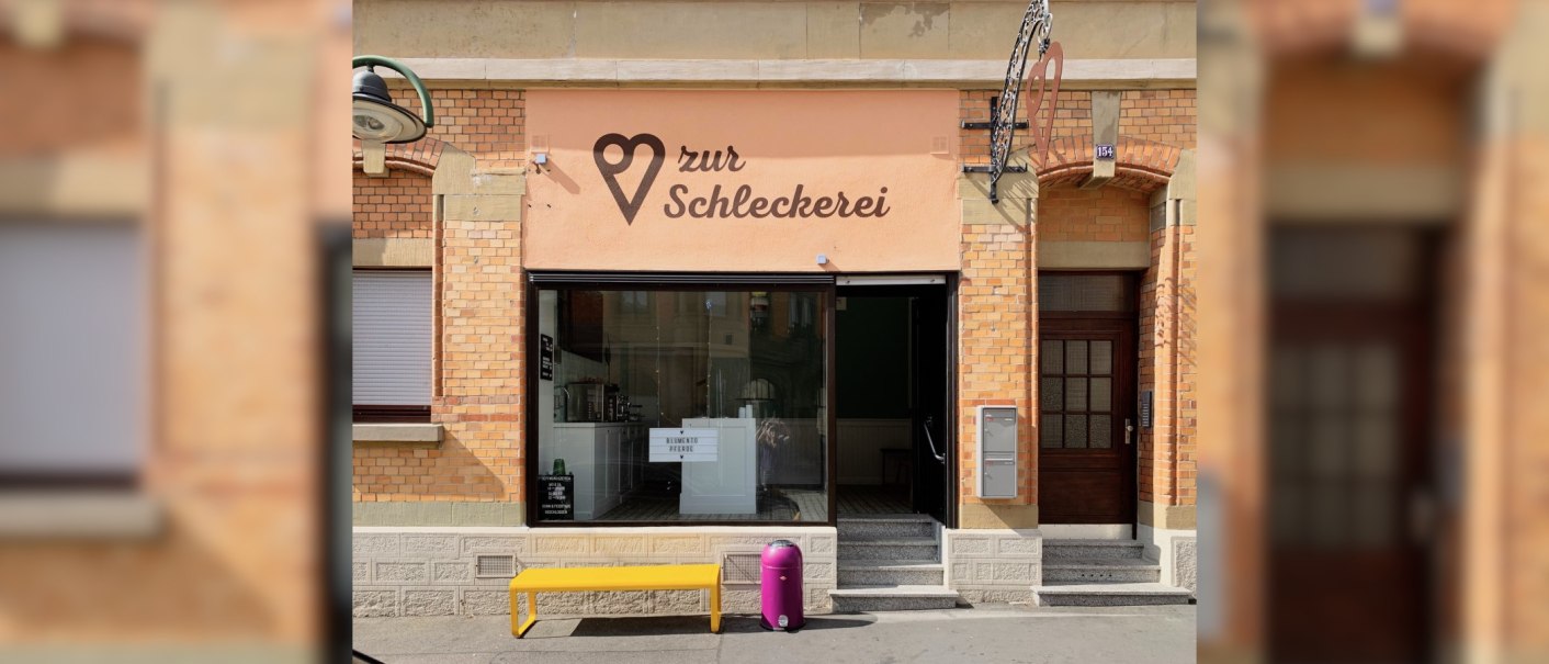 Gebäude mit der Aufschrift 'zur Schleckerei', gelbe Bank und lila Mülleimer davor., © Zur Schleckerei Gebäude mit der Aufschrift 'zur Schleckerei', gelbe Bank und lila Mülleimer davor., © Zur Schleckerei