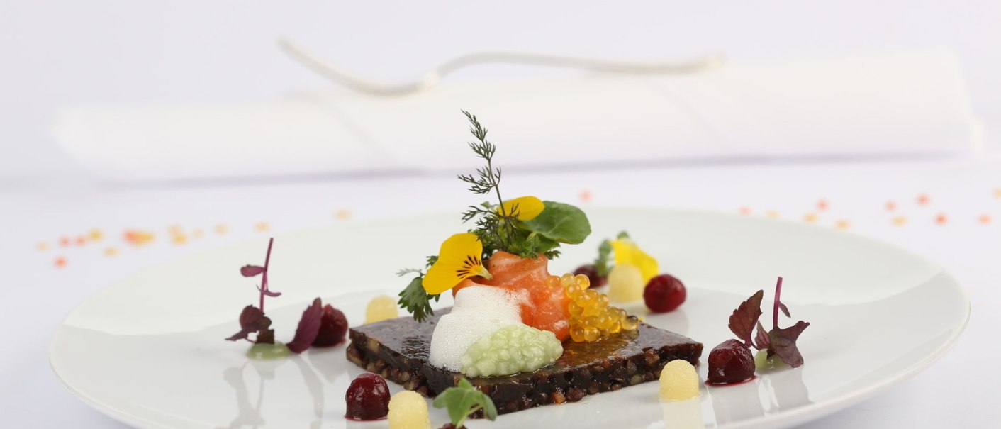 Ein kunstvoll angerichtetes Gourmetgericht mit essbaren Blüten und bunten Zutaten auf einem weißen Teller., © Landhaus Franz Feckl