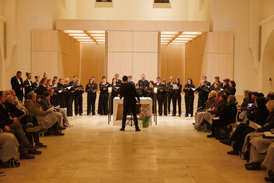 Ein Chor singt in einer Kirche, dirigiert von einer Person. Das Publikum sitzt auf beiden Seiten und hört zu. Die Atmosphäre ist feierlich., © Heiko Tiedmann