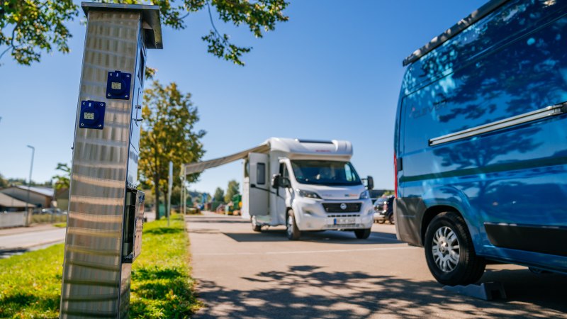 Wohnmobilstellplatz mit einem weißen Wohnmobil und einem blauen Van. Im Vordergrund eine Stromsäule, im Hintergrund Bäume und blauer Himmel., © Stuttgart-Marketing GmbH, Thomas Niedermüller