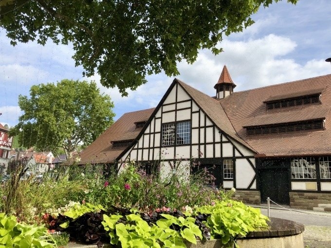 Fachwerkgebäude mit rotem Dach, umgeben von Bäumen und Blumenbeet im Vordergrund. Klarer Himmel und sonniges Wetter., © Stuttgart Marketing GmbH Fachwerkgebäude mit rotem Dach, umgeben von Bäumen und Blumenbeet im Vordergrund. Klarer Himmel und sonniges Wetter., © Stuttgart Marketing GmbH