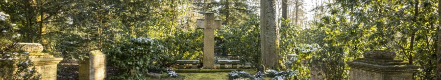 Ein ruhiger Friedhof mit einem gro&szlig;en Kreuz in der Mitte, umgeben von B&auml;umen und gr&uuml;ner Vegetation. Sonnenlicht f&auml;llt durch die Bl&auml;tter., &copy; Stuttgart-Marketing GmbH, Sarah Schmid