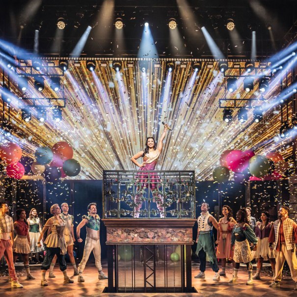 A dynamic stage scene from a musical with a woman in the center, surrounded by dancers, colorful lights and confetti., &copy; Johan Persson / Stage Entertainment