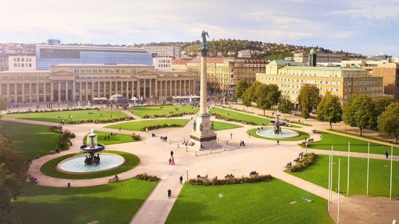 Der Schlossplatz in Stuttgart mit der Jubiläumssäule, umgeben von Grünflächen, Brunnen und historischen Gebäuden bei sonnigem Wetter., © Jean-Claude Winkler
