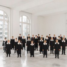 Jungenchor in schwarzen Roben mit weißen Kragen in einem hellen Raum mit großen Fenstern., © links im Bild