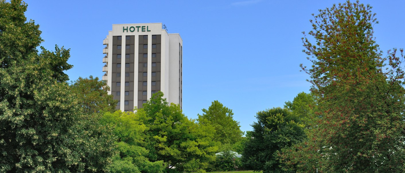 Hotel building behind trees in a park, blue sky., © AMBER HOTEL Leonberg / Stuttgart Hotel building behind trees in a park, blue sky., © AMBER HOTEL Leonberg / Stuttgart