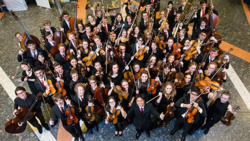 Jugendsinfonieorchester posiert mit Instrumenten in einem Innenraum. Die Musiker tragen formelle Kleidung und halten Geigen, Celli und Blasinstrumente., © Stefan Jetter Jugendsinfonieorchester posiert mit Instrumenten in einem Innenraum. Die Musiker tragen formelle Kleidung und halten Geigen, Celli und Blasinstrumente., © Stefan Jetter