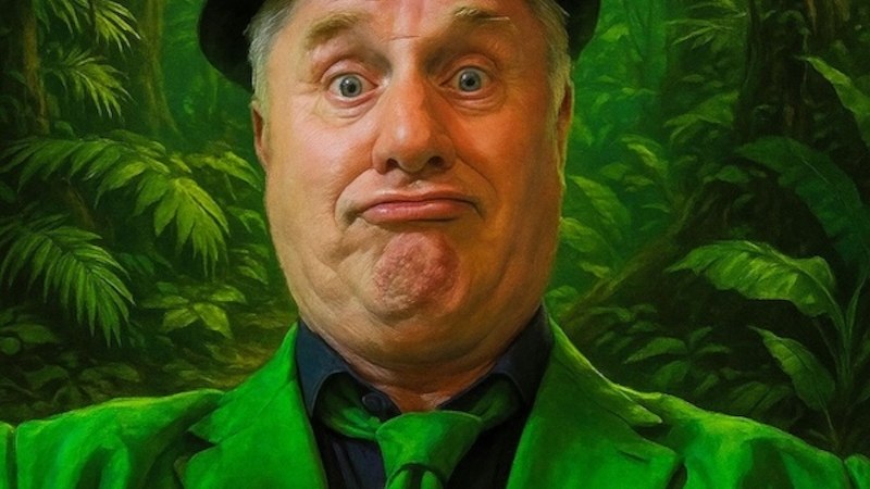 Ein Mann in grünem Anzug und Hut zieht ein lustiges Gesicht vor einem dschungelartigen Hintergrund., © Renitenztheater Stuttgart e.V. Ein Mann in grünem Anzug und Hut zieht ein lustiges Gesicht vor einem dschungelartigen Hintergrund., © Renitenztheater Stuttgart e.V.