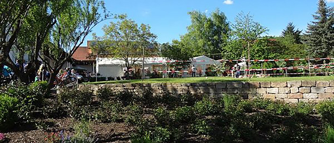 Ein Garten mit Bäumen und Menschen bei einem Fest. Im Hintergrund sind Zelte und ein Gebäude zu sehen. Der Himmel ist blau und sonnig., © Weingut Klopfer Ein Garten mit Bäumen und Menschen bei einem Fest. Im Hintergrund sind Zelte und ein Gebäude zu sehen. Der Himmel ist blau und sonnig., © Weingut Klopfer