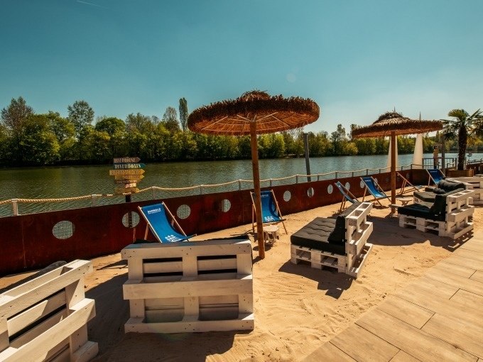 Beach area with sun loungers, parasols and pallet furniture on the riverbank. Trees and a clear sky can be seen in the background., &copy; Cool-Tours StattReisen