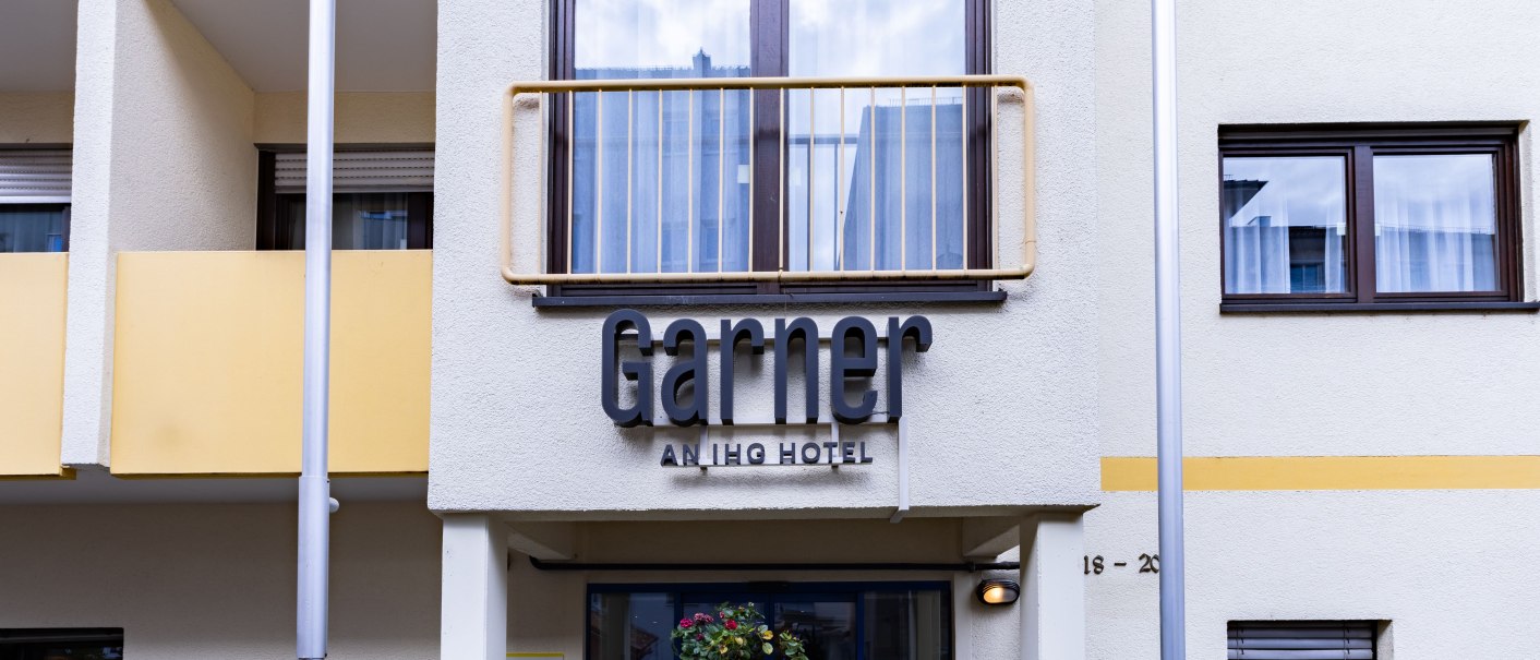 The facade of a hotel called "Garner." Yellow balconies and windows are visible. The entrance area is decorated with plants., &copy; Novum  Hospitality