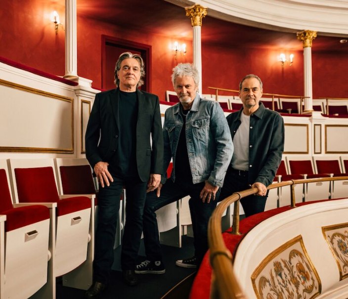 Three men pose in an elegant theater with red seats and golden decorations. They are wearing casual clothes and standing on a balcony., © C2 Concerts GmbH Three men pose in an elegant theater with red seats and golden decorations. They are wearing casual clothes and standing on a balcony., © C2 Concerts GmbH