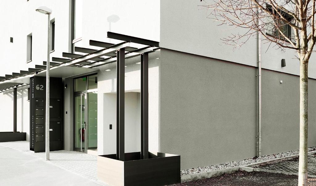 Moderne Gebäudeaußenansicht mit Glasfassade, Vordach und Baum. Die Fassade ist in neutralen Farben gehalten, mit klaren Linien und minimalistischem Design., © livisit bergapartments