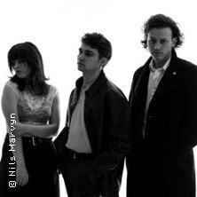 Drei Personen in Schwarz-Weiß, stilvoll gekleidet, stehen vor einem hellen Hintergrund. Eine Frau und zwei Männer blicken ernst., © links im Bild Drei Personen in Schwarz-Weiß, stilvoll gekleidet, stehen vor einem hellen Hintergrund. Eine Frau und zwei Männer blicken ernst., © links im Bild