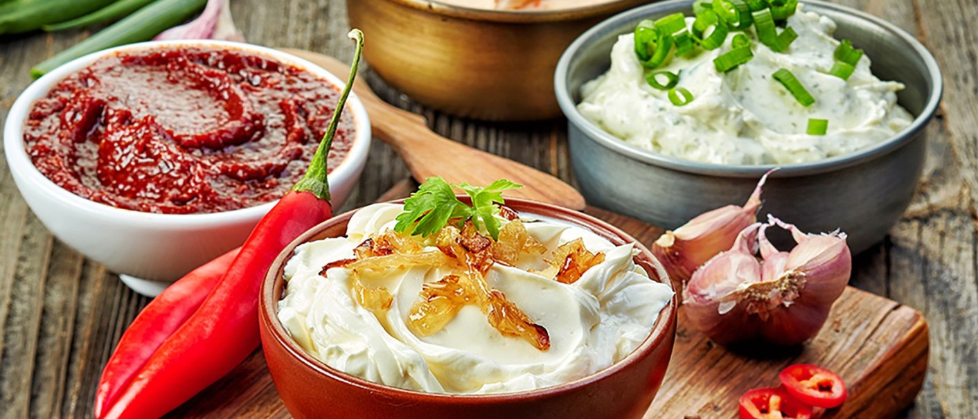Various dips in bowls, surrounded by red chili peppers and garlic arranged on a wooden table., &copy; MASEVEN Stuttgart SI-Centrum