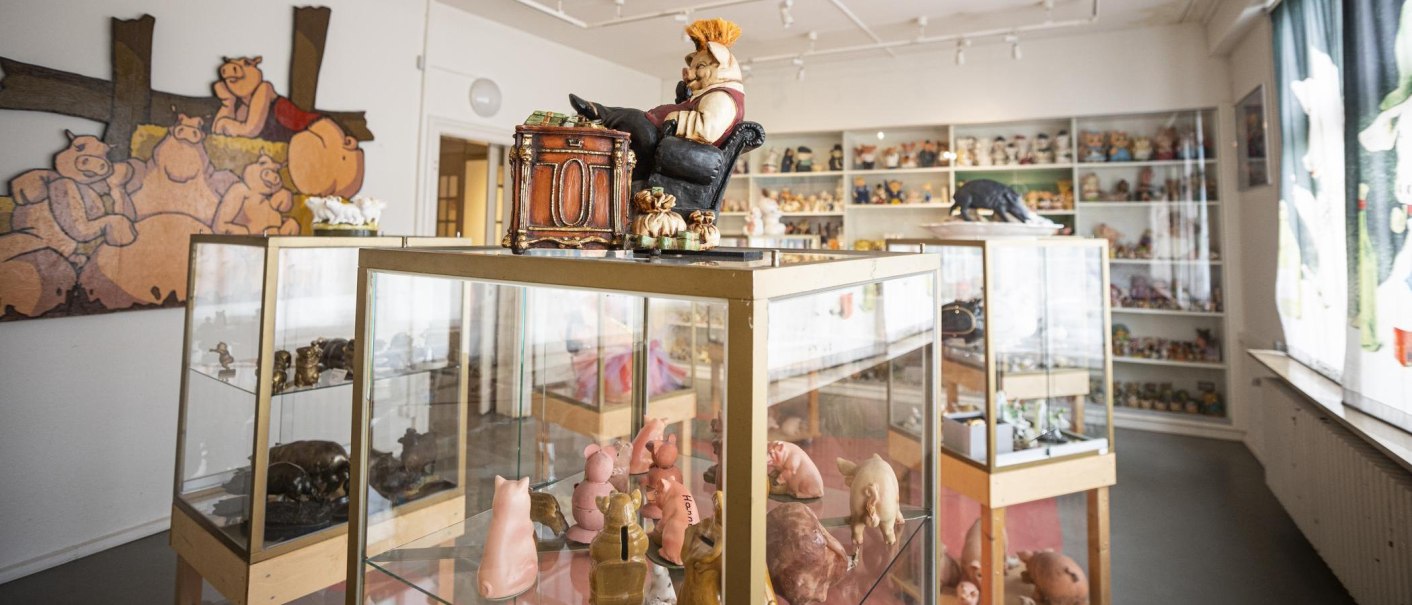 Ein Raum im Schweinemuseum Stuttgart mit Vitrinen voller Schweinefiguren und einem großen Wandbild von Schweinen., © Stuttgart-Marketing GmbH, Sarah Schmid