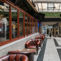 A cozy courtyard with red leather armchairs, decorative plants and a glass roof. A person enters the area in the background., &copy; SMG Stuttgart Marketing GmbH - Sarah Schmid
