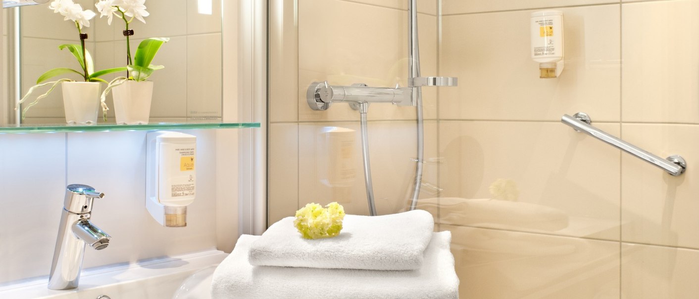 A modern bathroom with a shower, sink, white towels, and orchids on a shelf., &copy; TOMAS