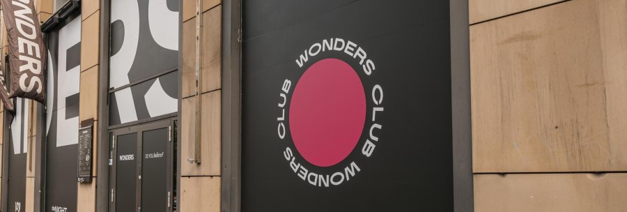 Eingang des Wonders Club mit großem Logo und Schriftzug an der Fassade. Schwarze Türen und ein pinker Kreis mit dem Text 'Wonders Club'., © Stuttgart Marketing GmbH, Sarah Schmid
